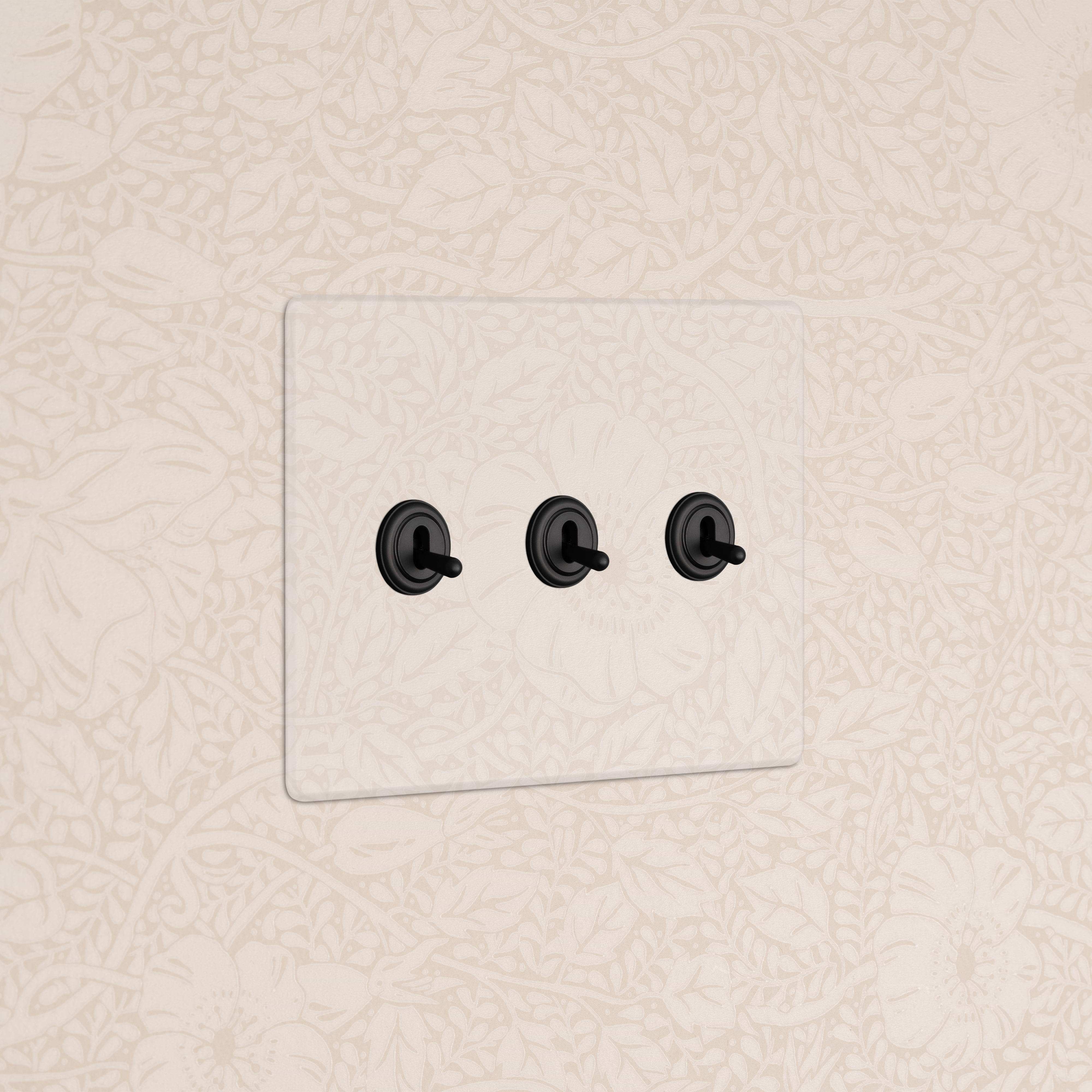 Kew 3G Toggle Switch in Clear Bronze finish with three black toggles, mounted on a beige patterned wall.