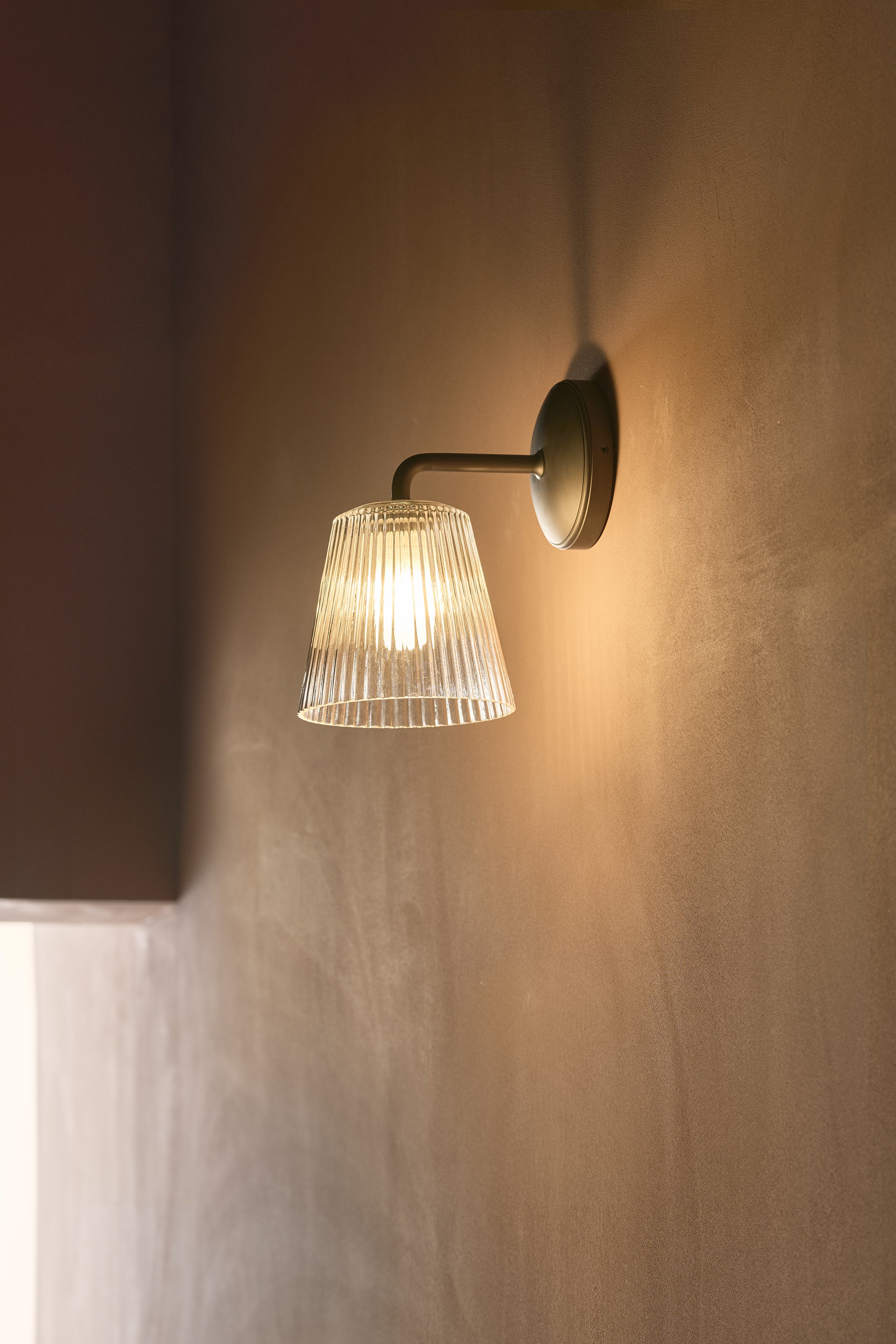 Richmond Medium Wall Light with fluted glass shade and bronze finish, mounted on a beige wall.
