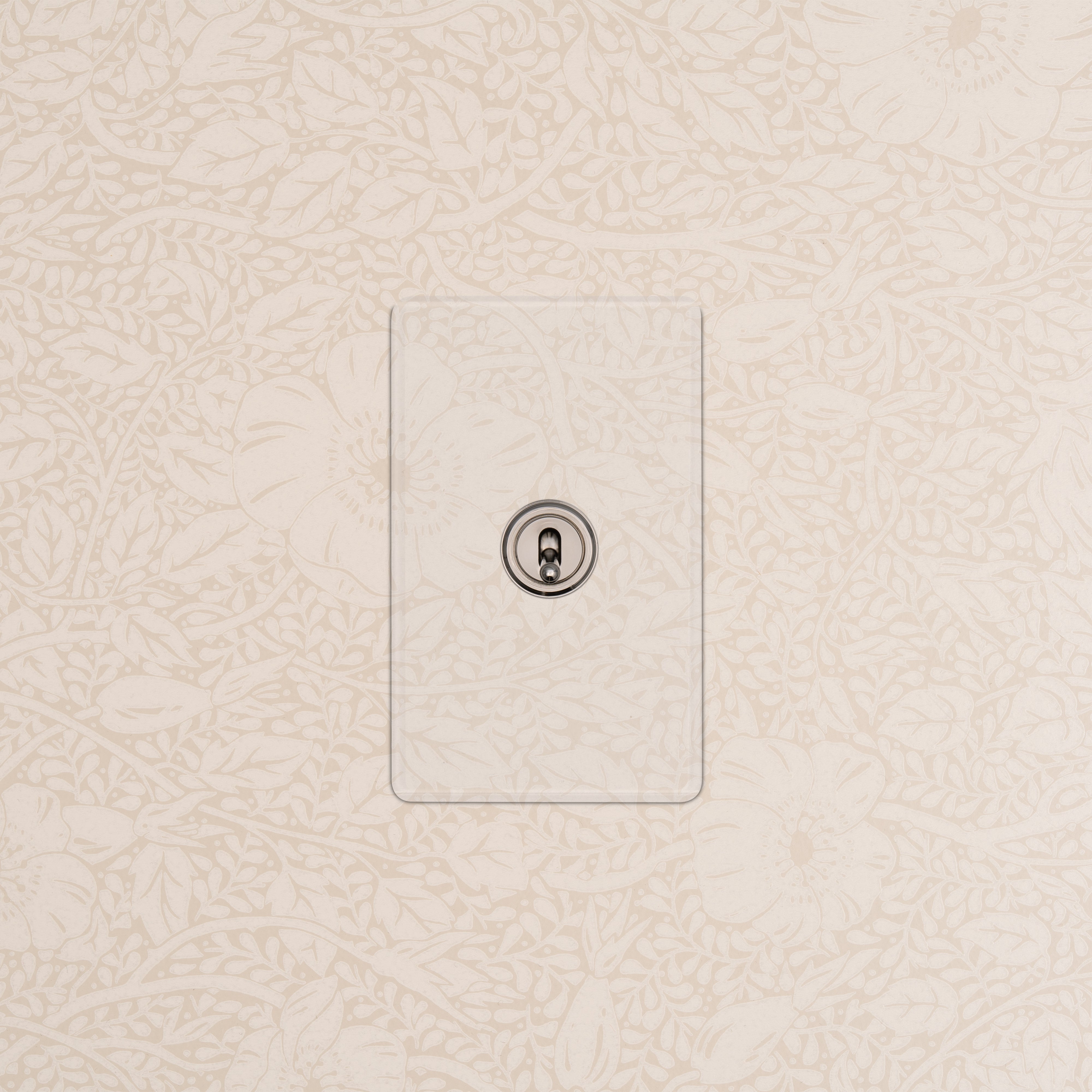 Kew 1G Smart Retractive Toggle Switch in Clear Polished Nickel mounted on a beige floral-patterned wall.