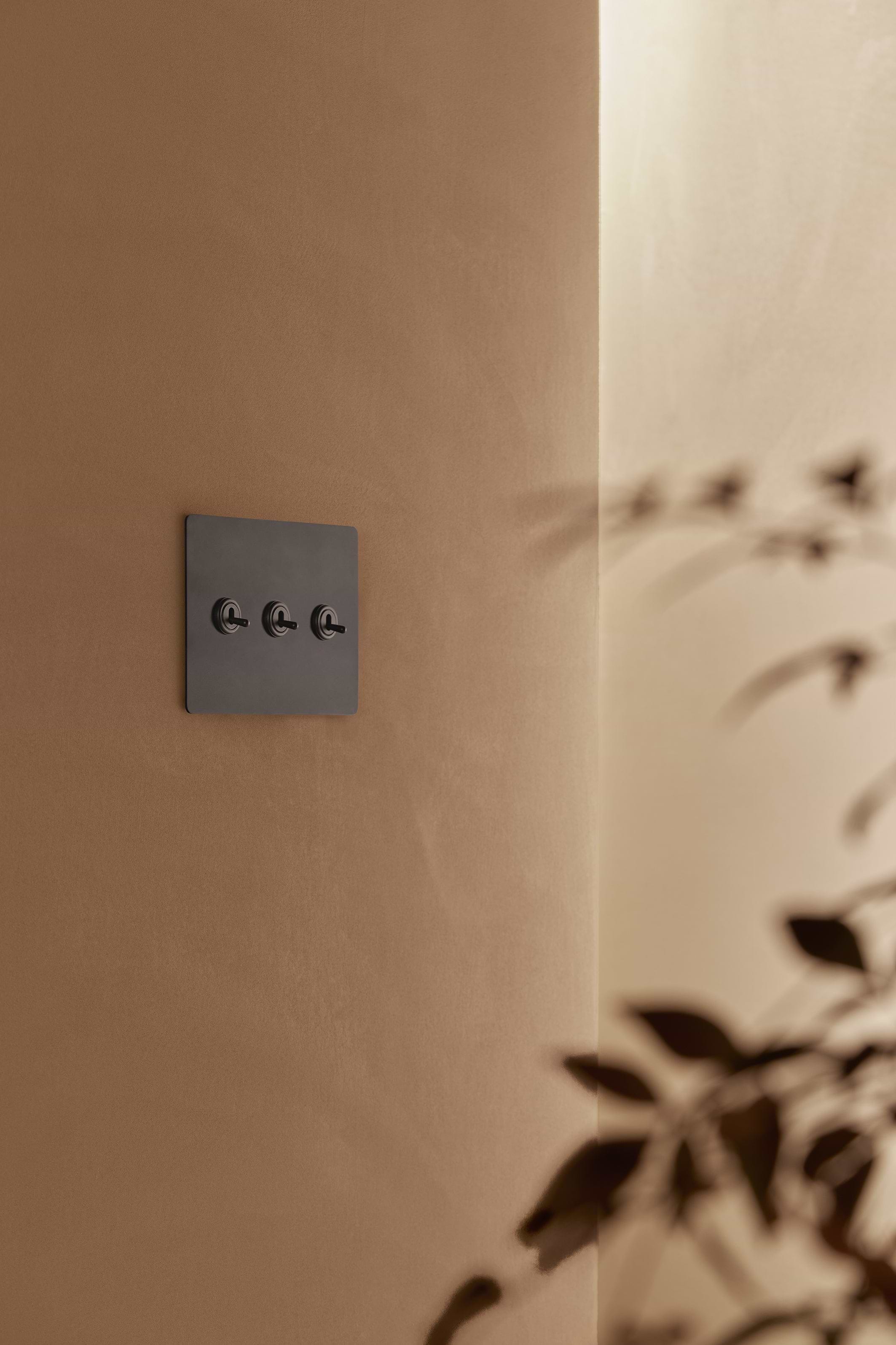 Kew 3G Toggle Switch in bronze with three toggles, mounted on a beige wall.