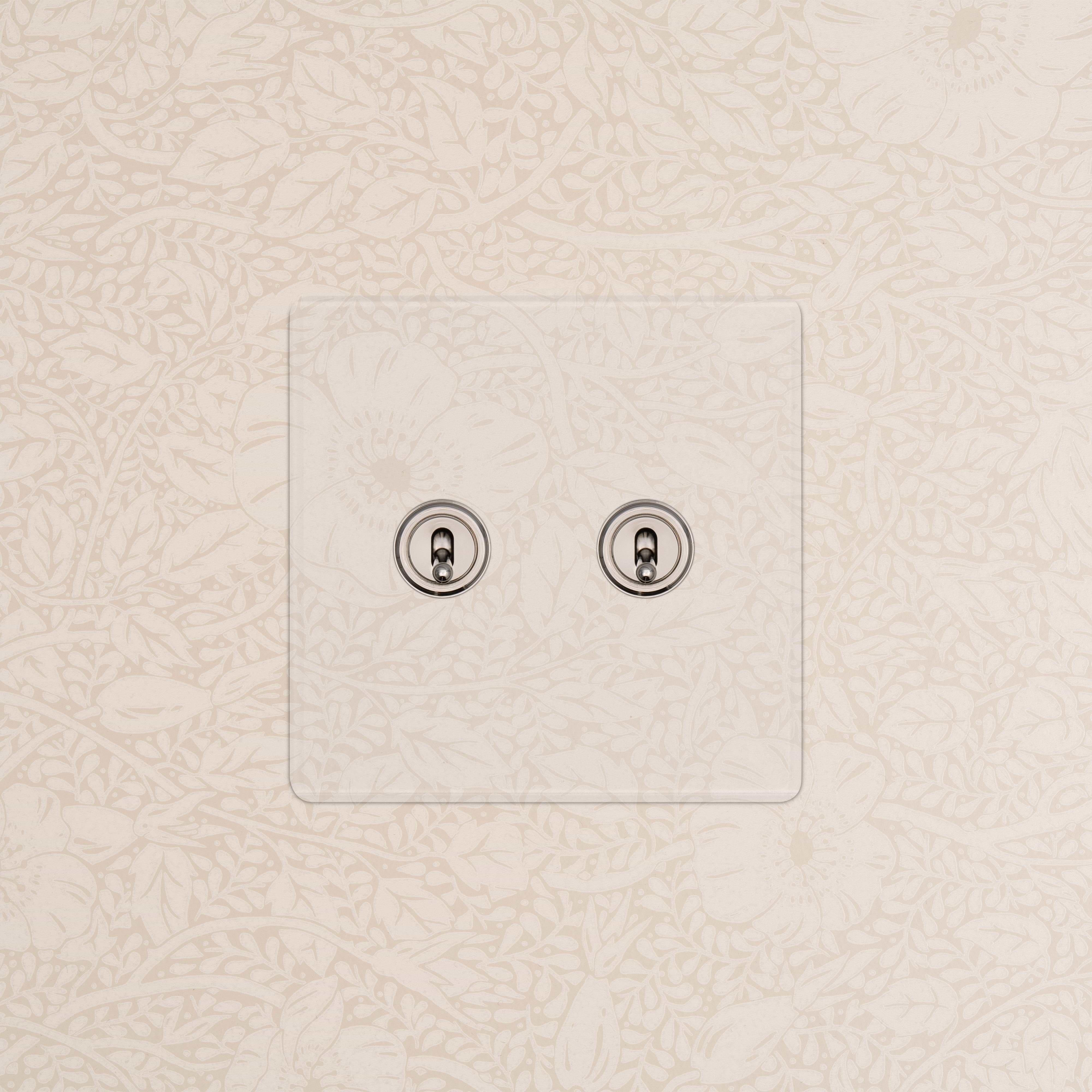 Kew 2G Toggle Switch in Clear Polished Nickel finish with two chrome toggles on floral-patterned wallpaper.