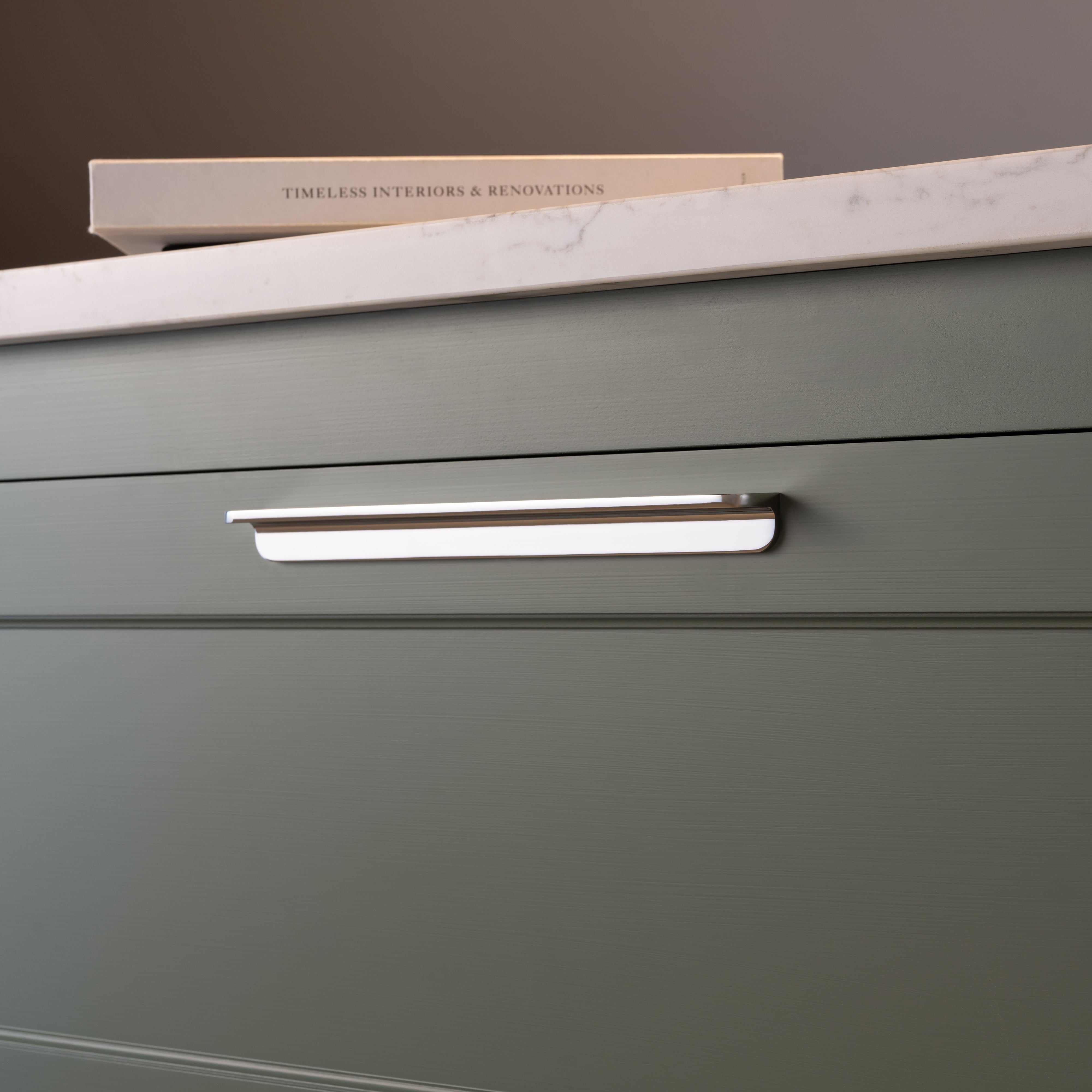 Large polished nickel Oxford Furniture Handle fitted on a matte green drawer beneath a white marble countertop.