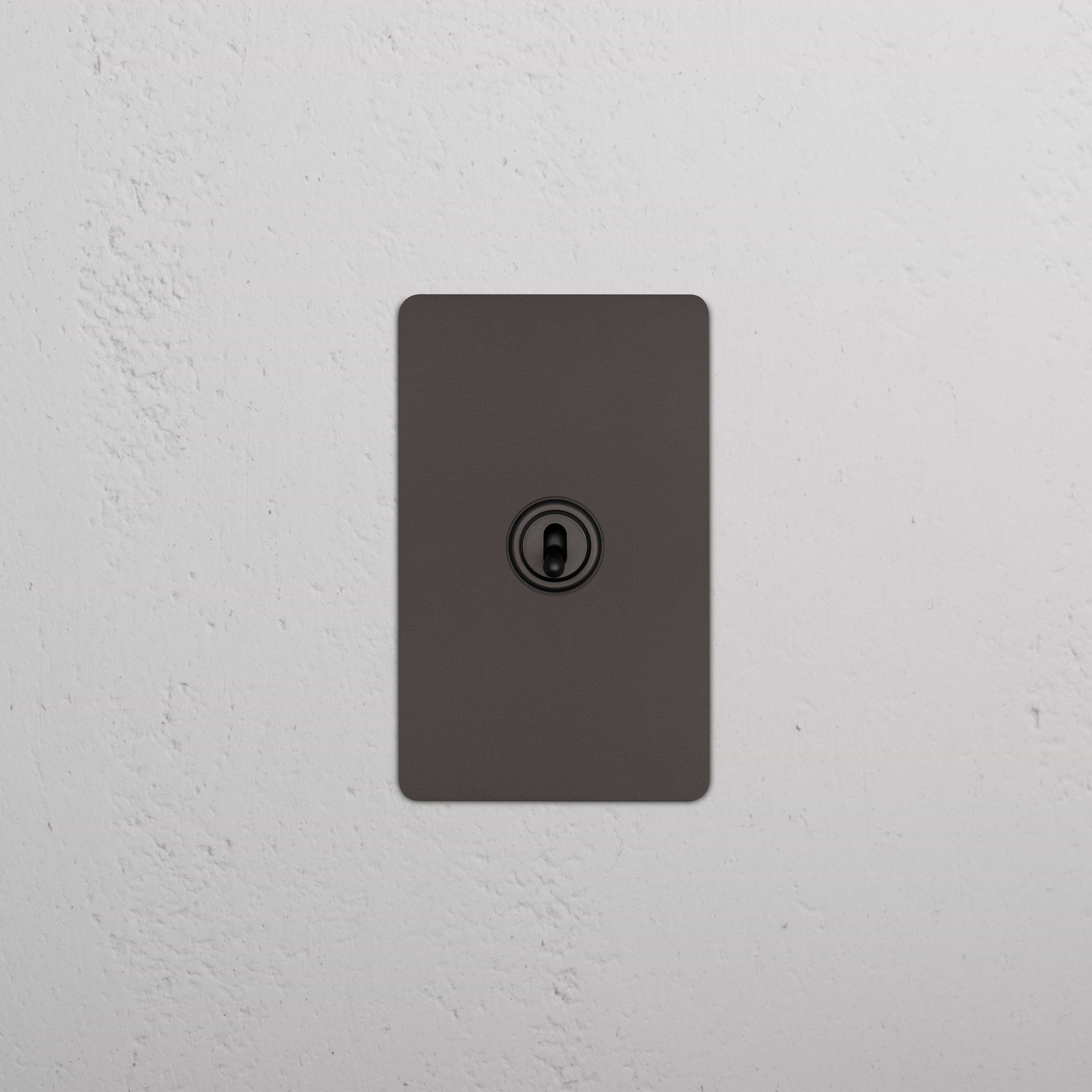 Kew 1G Dimming Retractive Toggle Switch in bronze, single gang, shown mounted on a white textured wall.