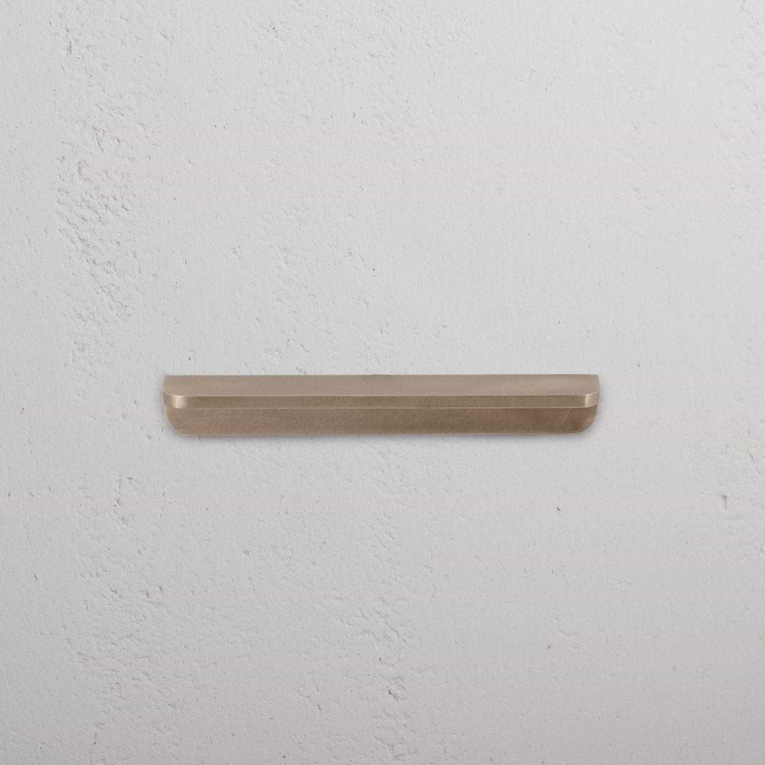Oxford Furniture Handle Small in antique brass, mounted on a textured white wall.
