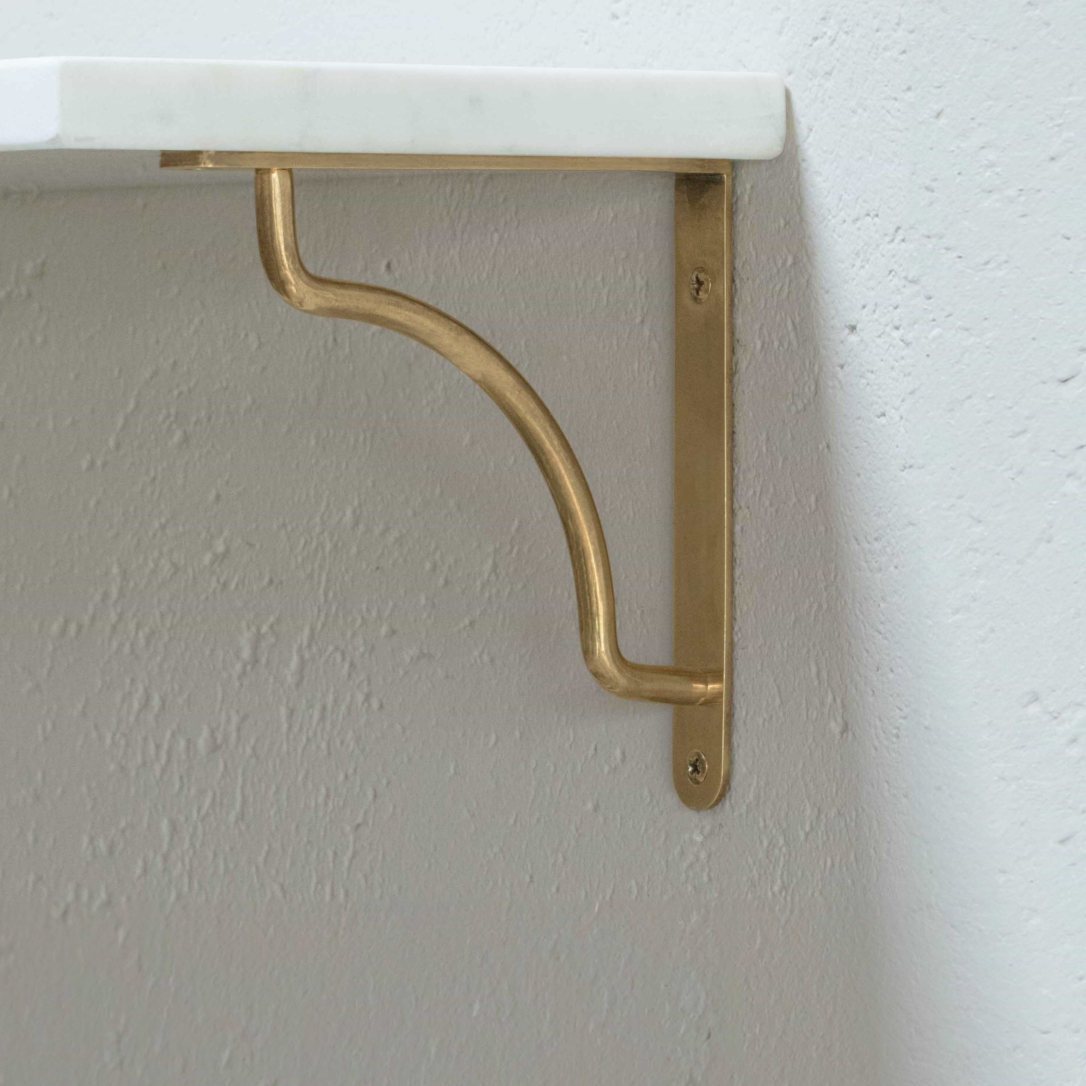 Small Kilburn Shelf Bracket in antique brass with a curved design, mounted on a light textured wall.