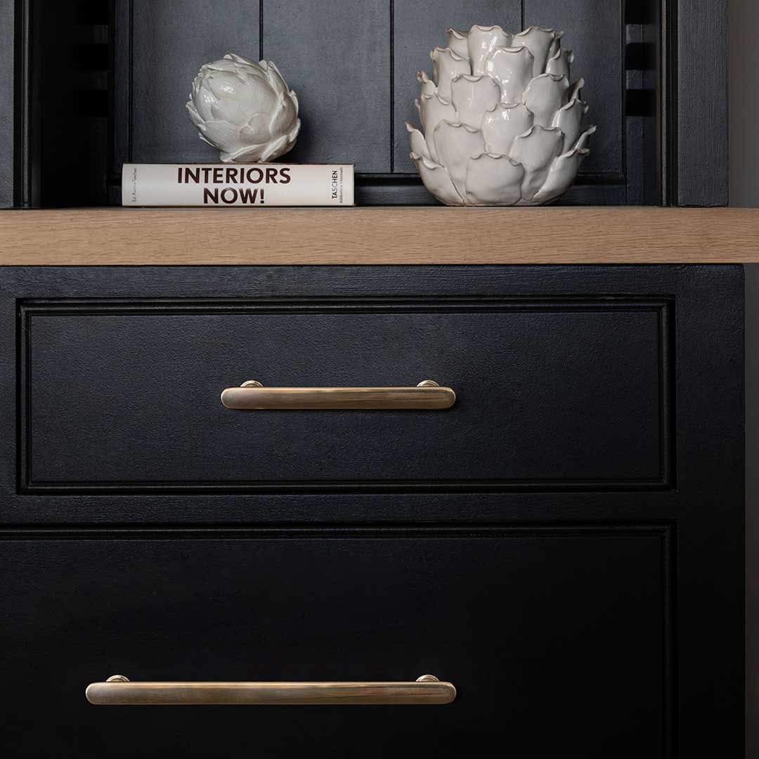 Medium antique brass Milliner furniture handle mounted on a black cabinet with decorative items on top.