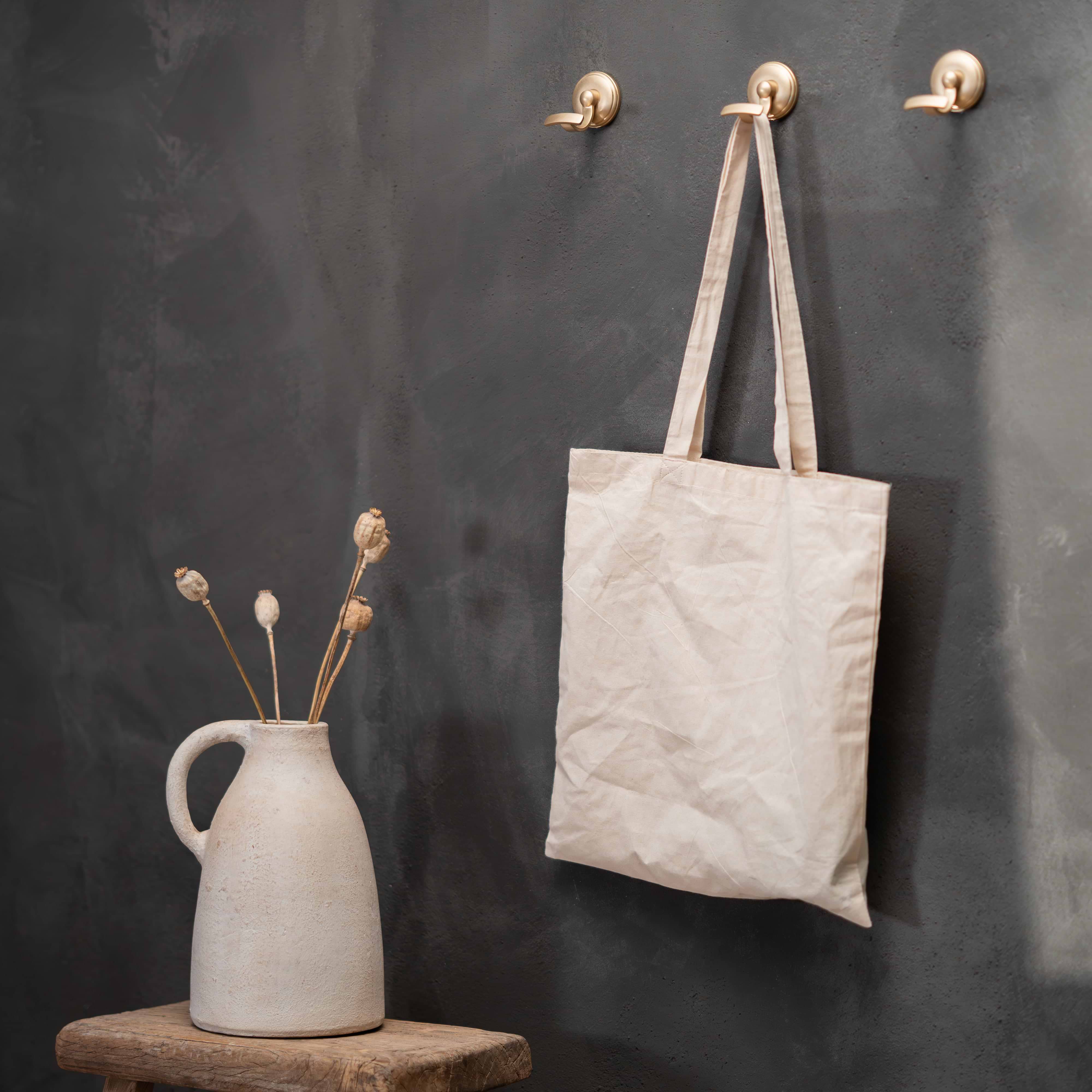 Portland Hook in antique brass mounted on a dark wall, shown holding a beige canvas tote bag.