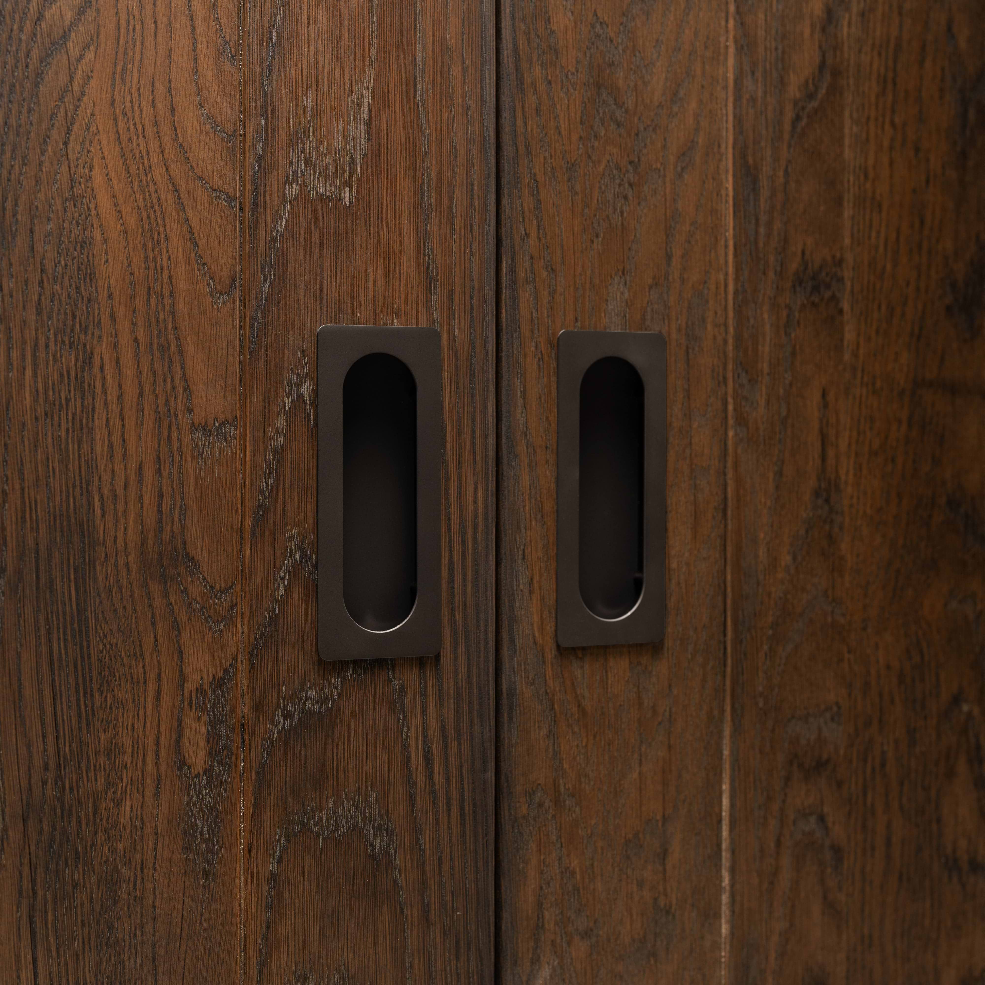 Close-up of two Regent Recessed Medium Pulls in bronze on dark wood sliding doors, showing their modern design.