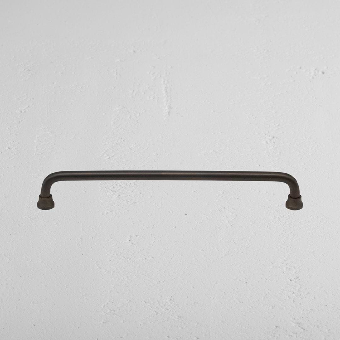 Medium bronze Sycamore Furniture Handle mounted horizontally on a textured white wall.