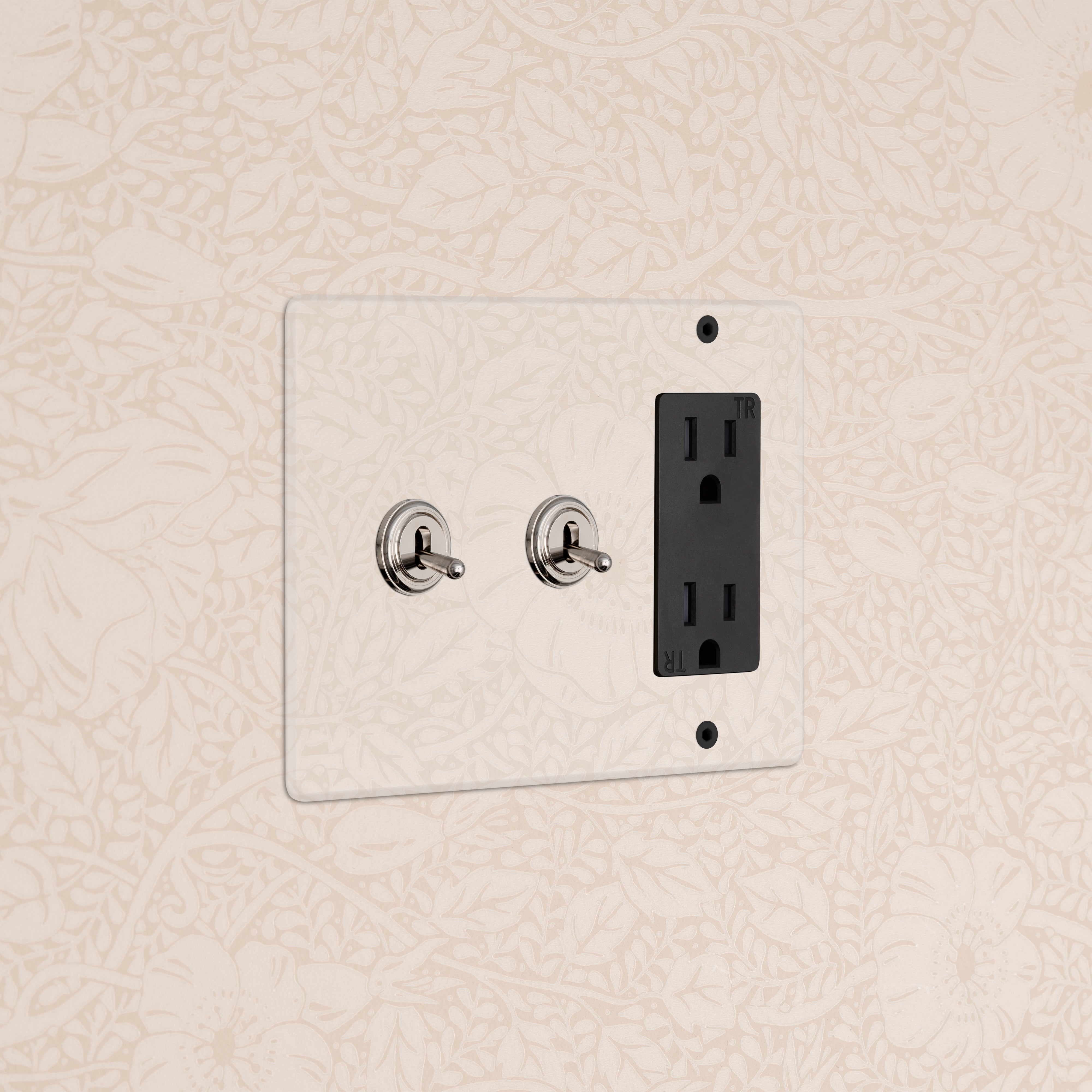 Kew 3G 2x Toggle Switch & Outlet in clear polished nickel black finish, mounted on floral wallpaper.