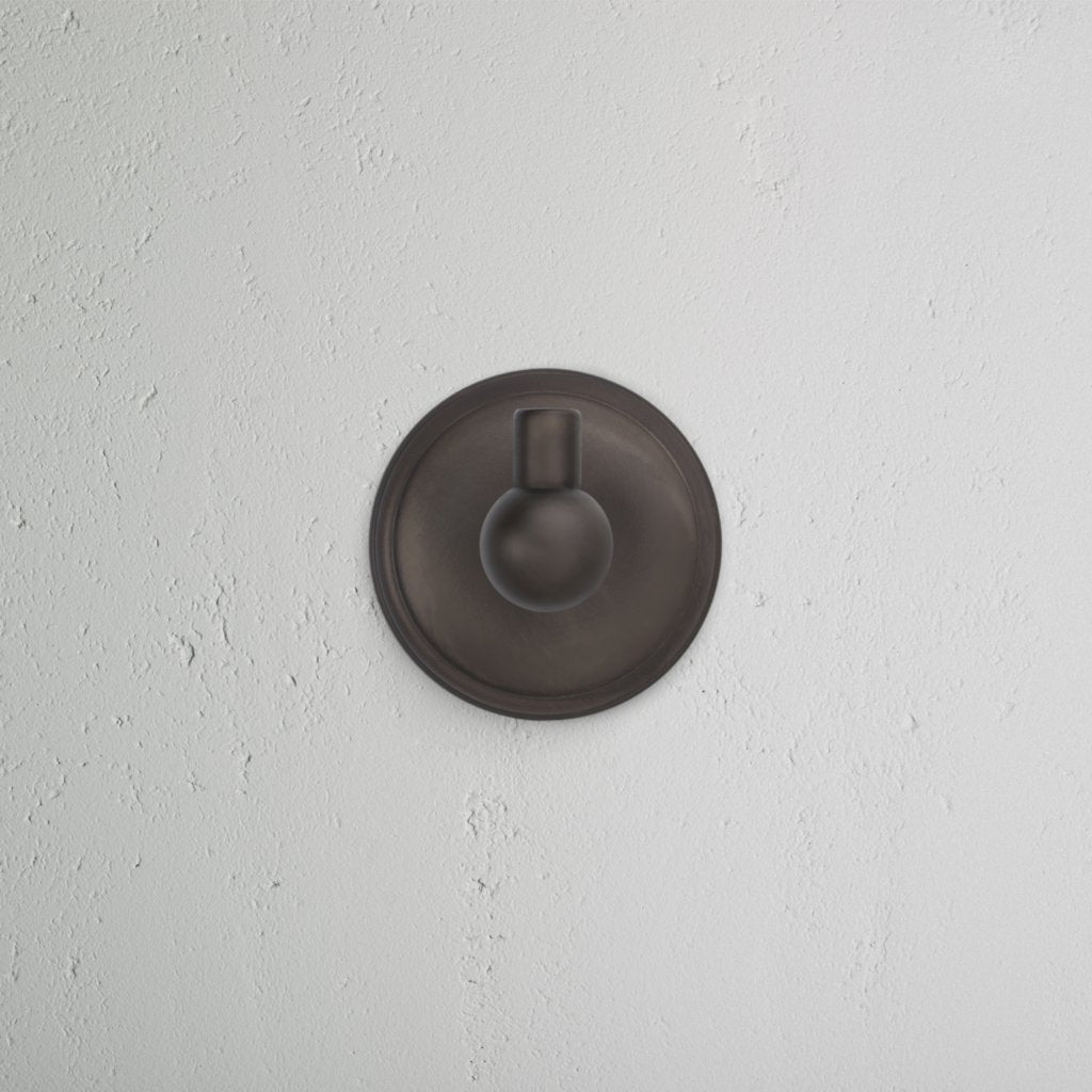Hyde Hook - Bronze: a modern, round bronze wall hook with a circular base and short peg, mounted on white wall.