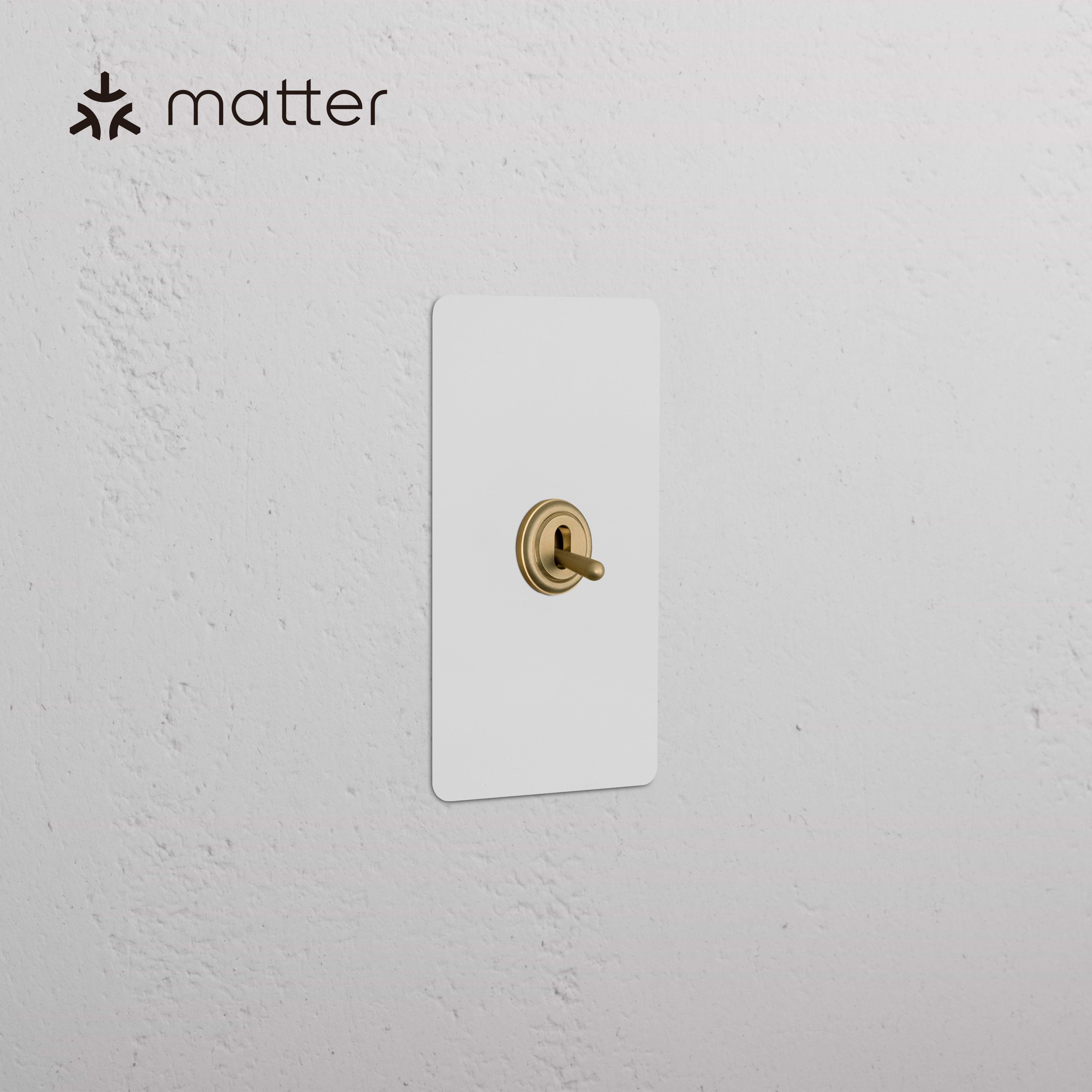 Kew 1G Smart Retractive Toggle Switch in paintable antique brass finish, mounted on a white wall.