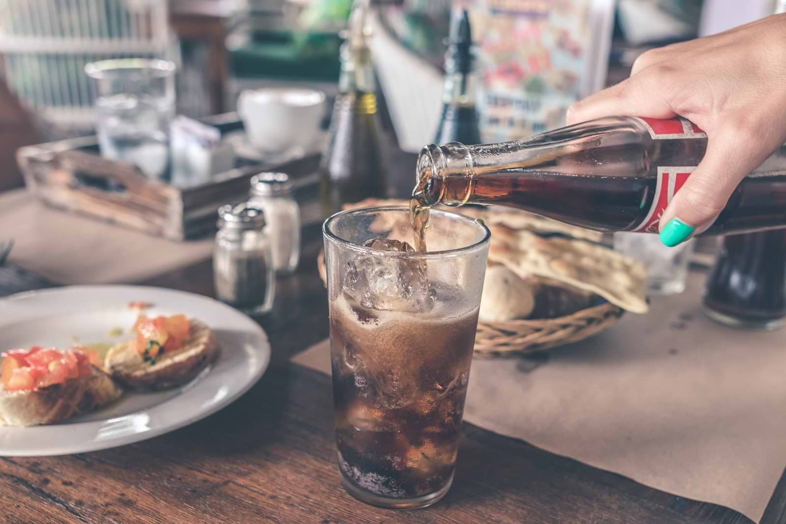 How to get rid of bloating: A hand pours a bottle of cola into a glass