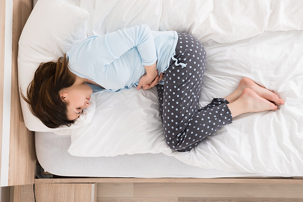 Woman laying in bed while holding her belly, in need of natural treatments for PMS