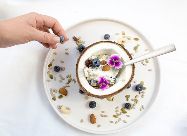 Kefir yogurt inside a coconut, surrounded by fruit, nuts, and flowers