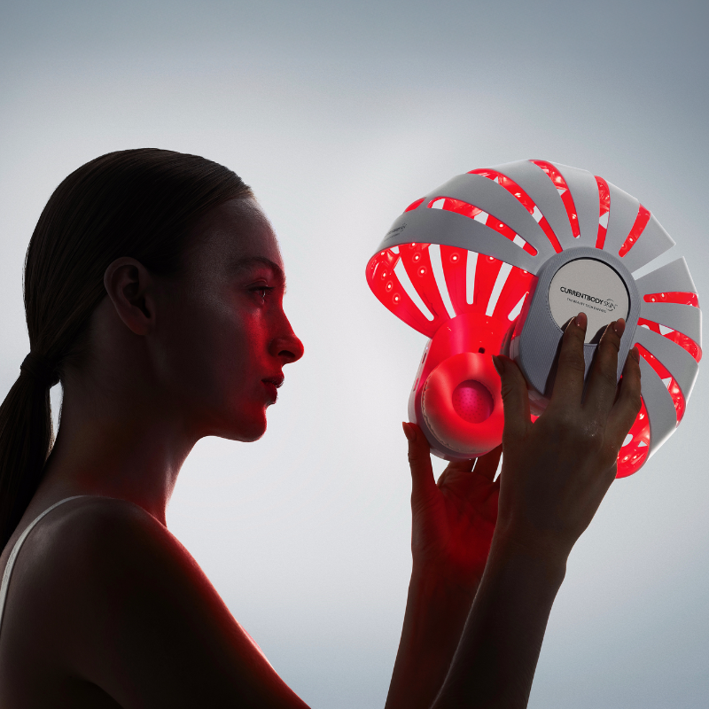 Woman holding the CurrentBody LED red light helmet for scalp health