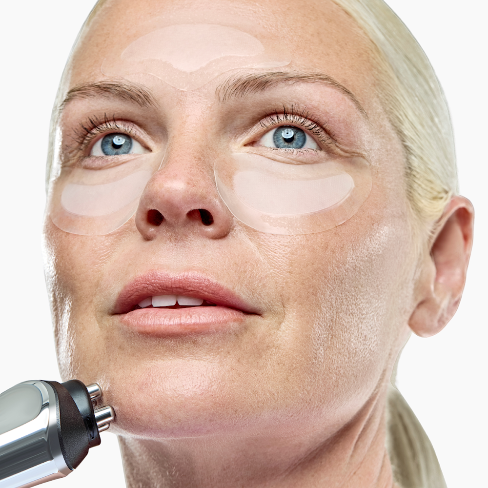 Woman wearing microneedling patches holding rf device to her face
