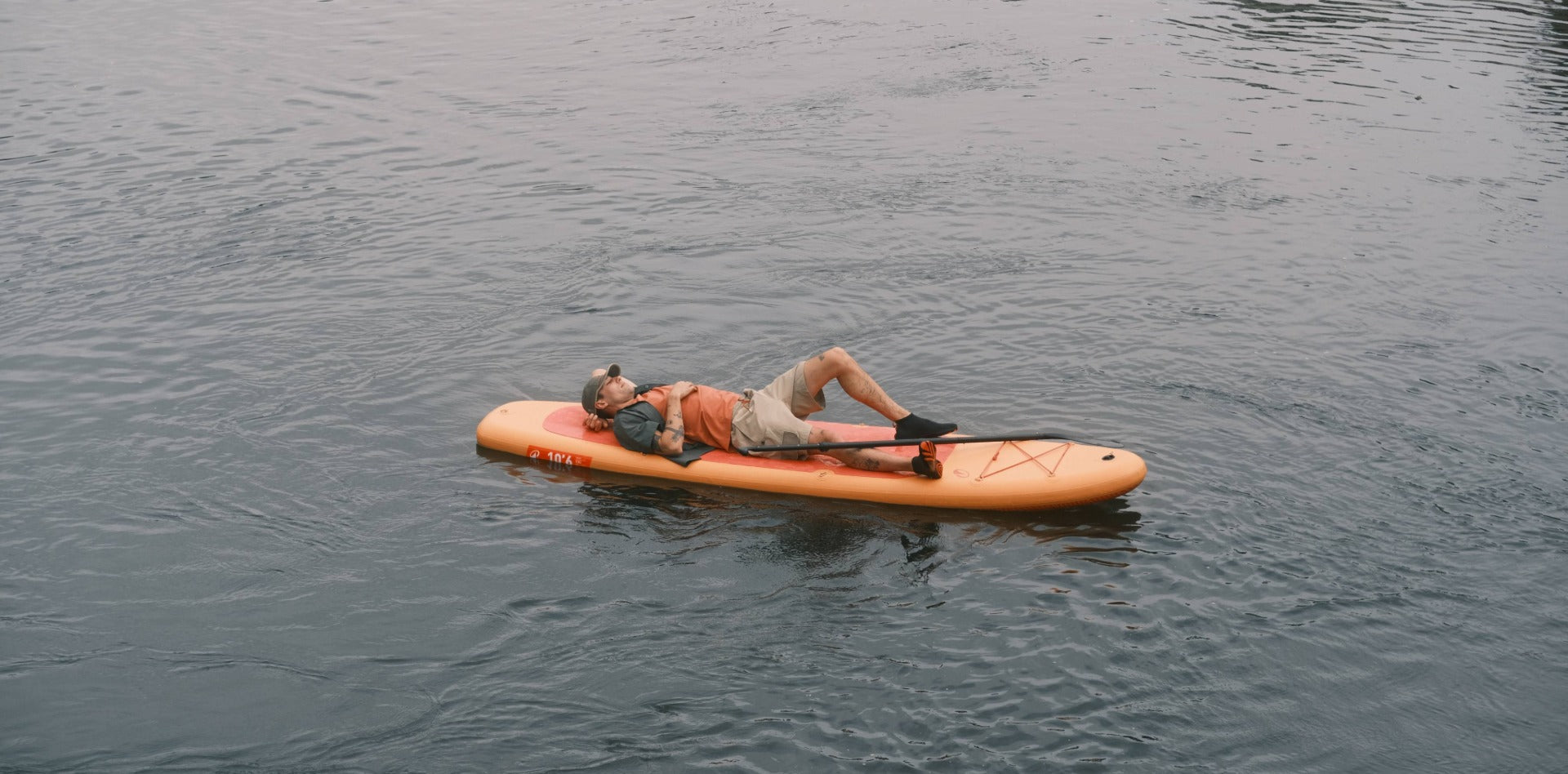 A man relaxing on an orange paddleboard on calm water in the Sealskinz Father's Day Gift Guide 2026.