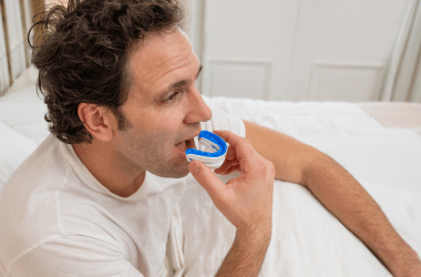 Man using a dental mouthguard while sitting on a bed, focusing on oral care and dental health