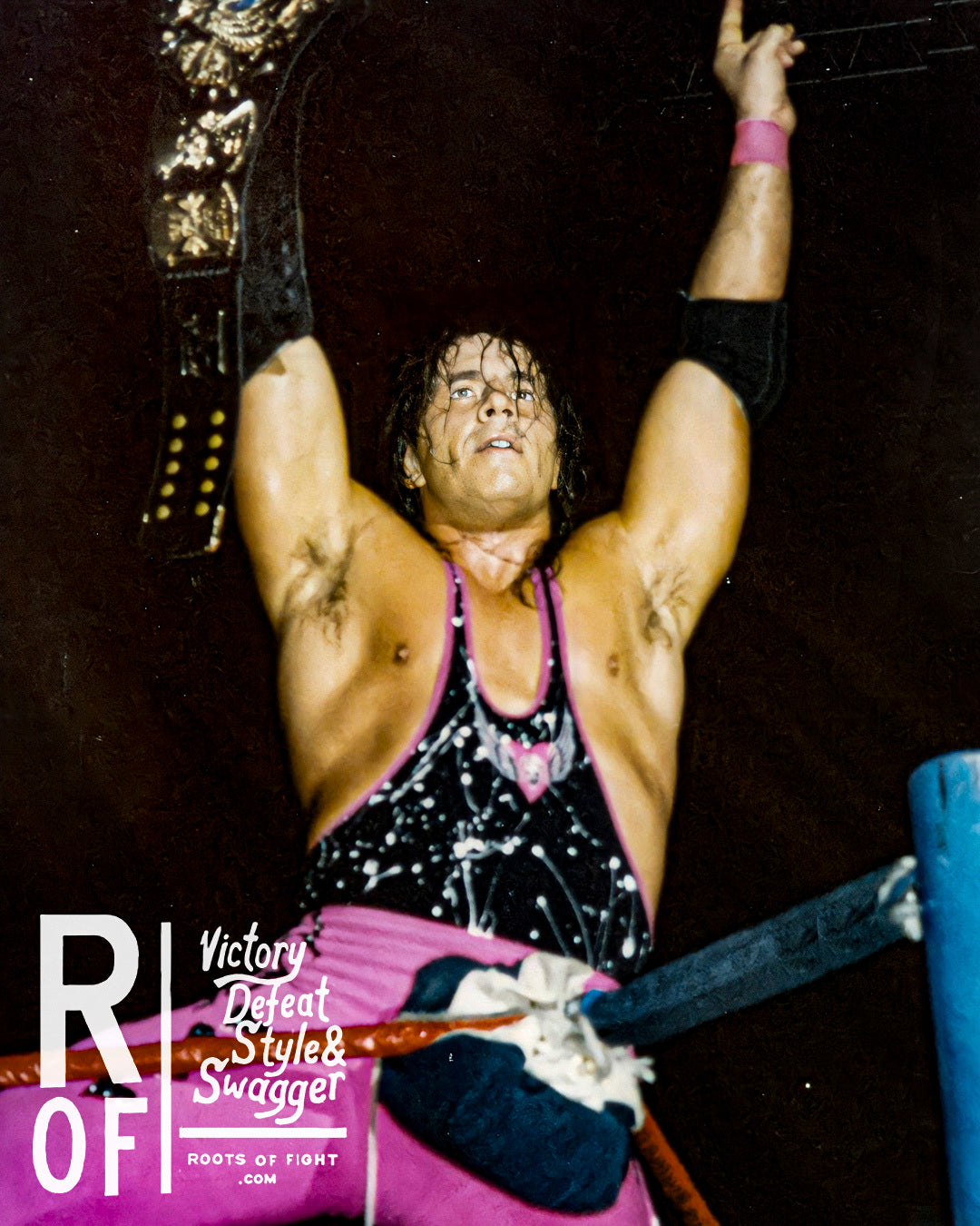 Wrestler in pink outfit celebrating in the ring with a championship belt overhead.