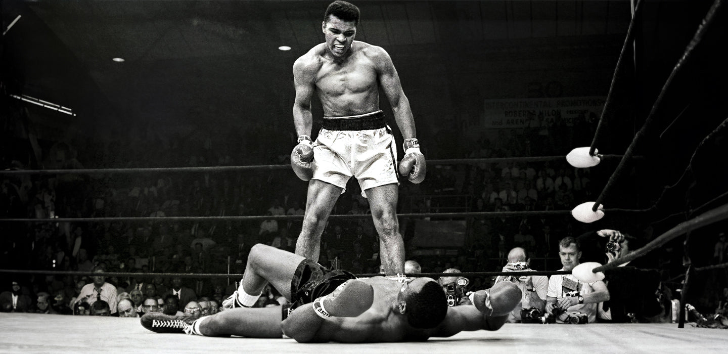 A boxer stands over his opponent who is lying on the boxing ring floor.