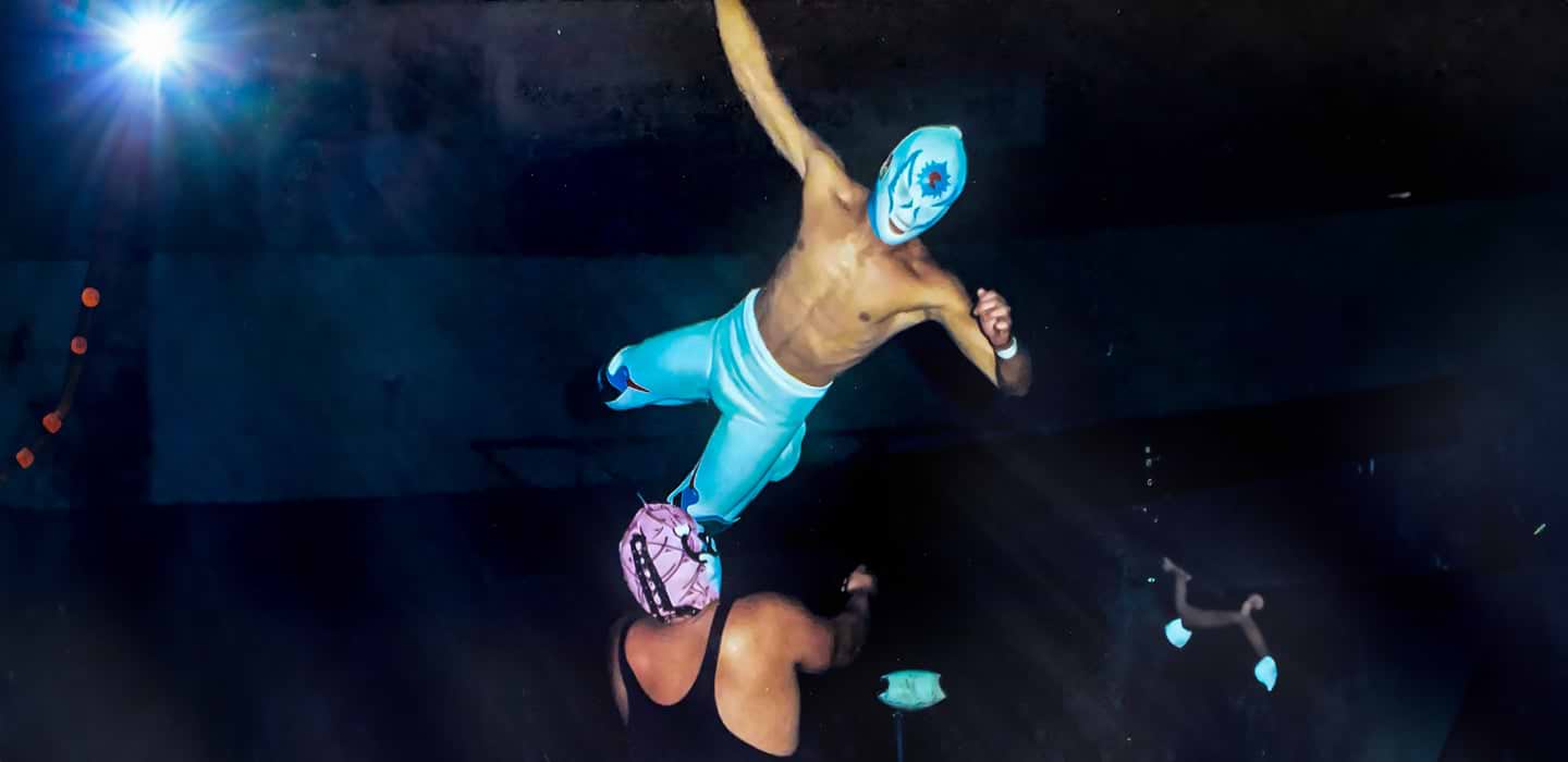 Masked wrestler flying in the air during a dramatic move in a wrestling match.