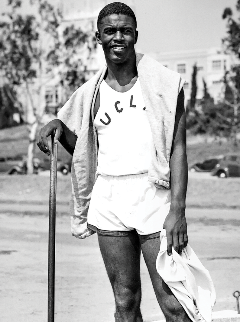 Young athlete wearing a UCLA tank top, holding an athletic pole, smiles outdoors.