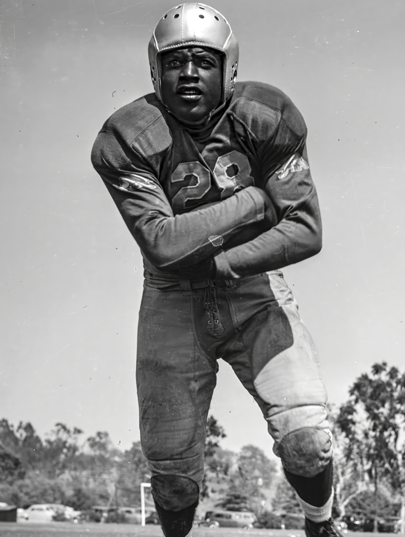 Football player in vintage uniform, wearing helmet, number 28, posing on a field.