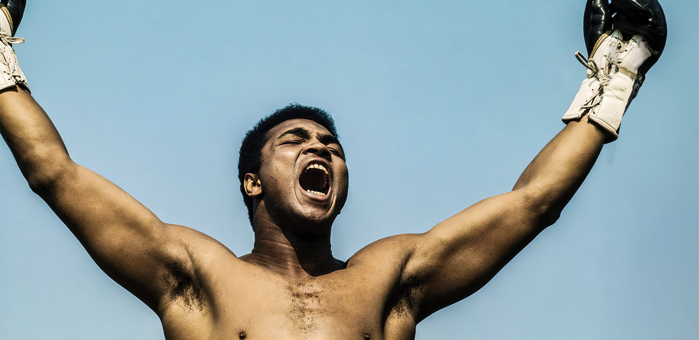 Boxer triumphantly raising arms and shouting against a clear blue sky.