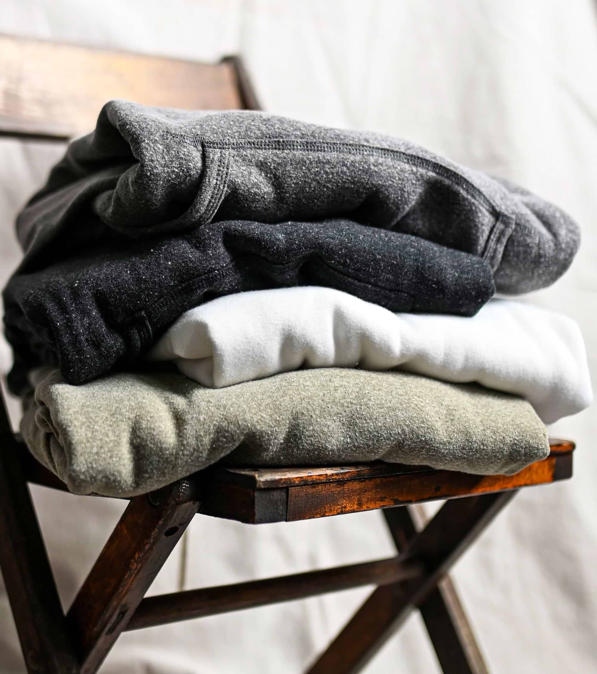 Folded clothes in shades of gray and white stacked on a wooden chair.