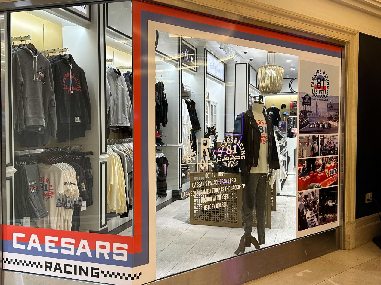 Storefront window displaying racing-themed clothing and memorabilia with 'Caesars Racing' signage.