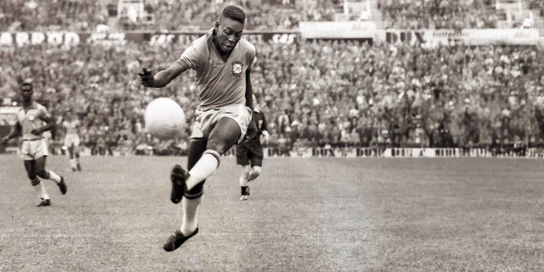 A black-and-white photo of a soccer player kicking a ball during a match.