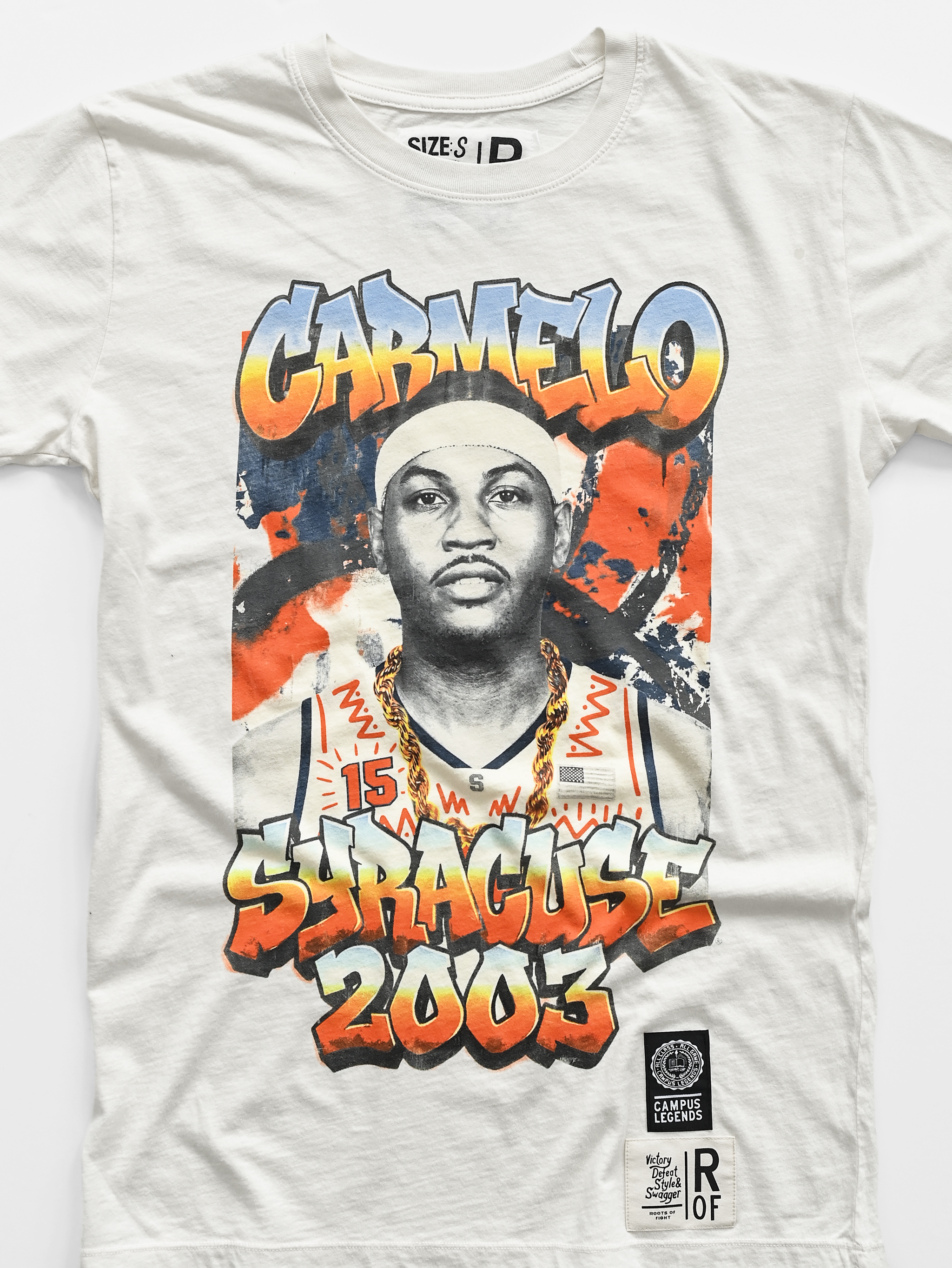 A white graphic t-shirt featuring a stylized portrait of Carmelo Butler with the text 'CARMELO' and 'SYRACUSE 2003' in graffiti-style lettering. The shirt includes a black circular 'Campus Legend' patch on the lower right side.