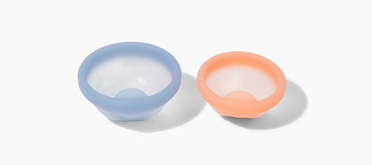 Two reusable silicone menstrual discs in blue and peach displayed on a light gray background