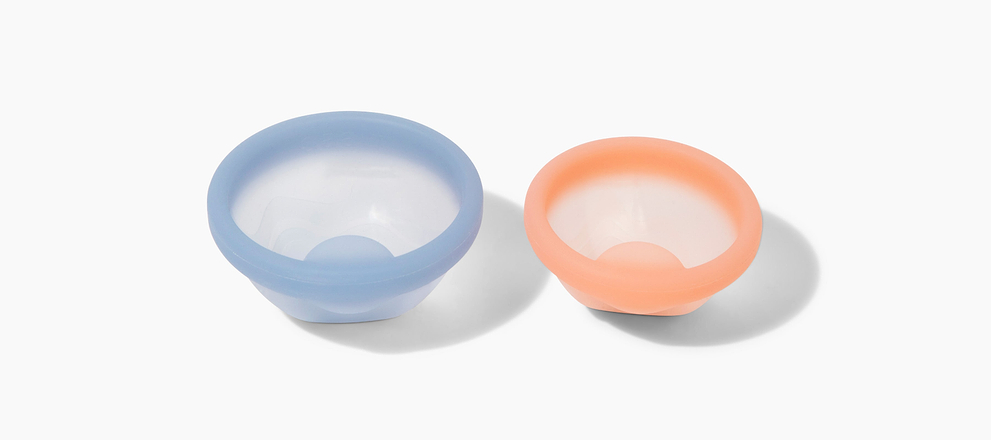 Two reusable silicone menstrual discs in blue and peach displayed on a light gray background