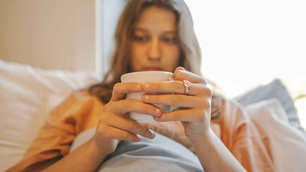 Nauseous Woman Lying in Bed, Sipping Warm Tea