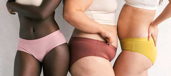 Three women in colorful period underwear posing together to showcase inclusive sizing and body diversity.