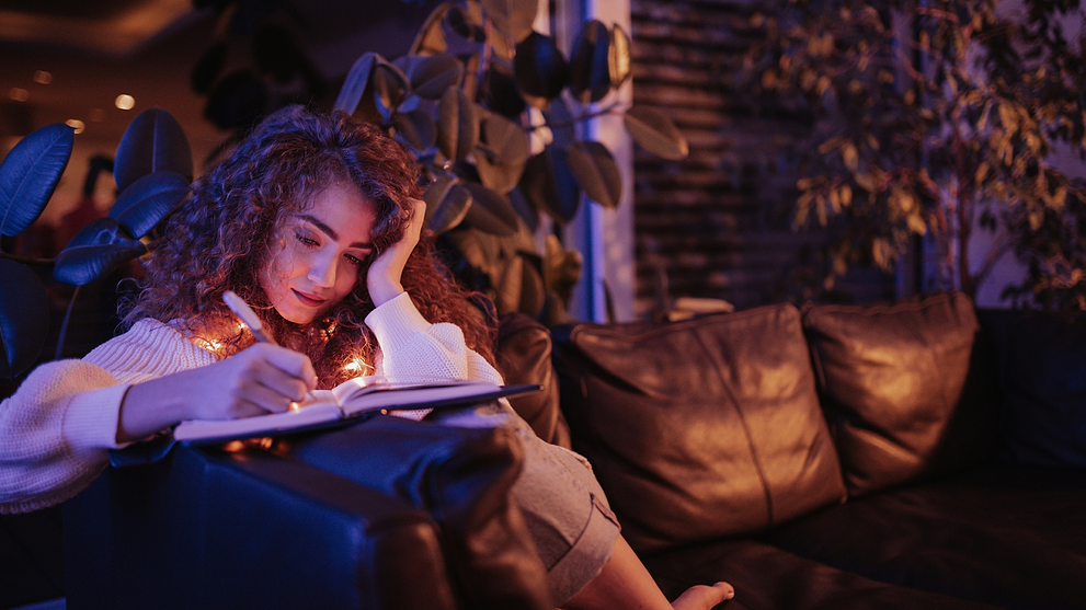 Woman With Curly Hair Journaling Her Illness And Menstrual Cycle On A Couch