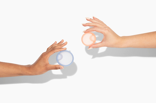 Two hands holding reusable menstrual discs against a light background with soft shadows.