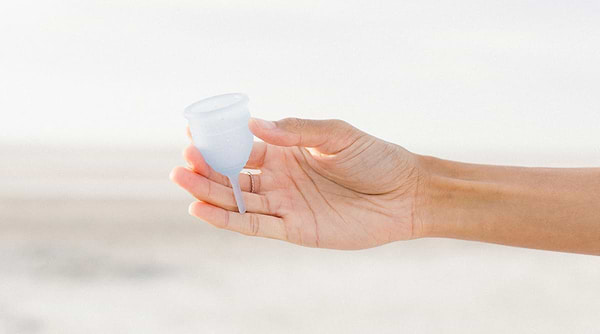 Hand holding blue menstrual cup on the beach.