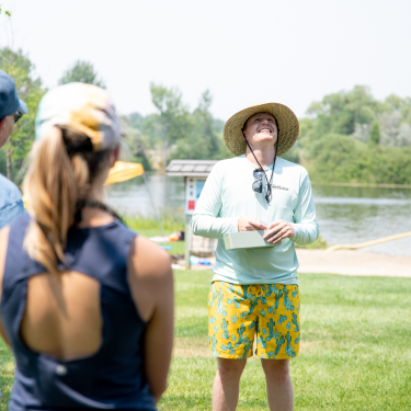 male wearing teal blue shirt, yellow colorful swim trunks leading a team event