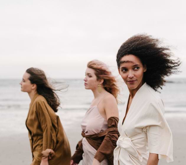 three females on the beach with their hair getting blown by the wind