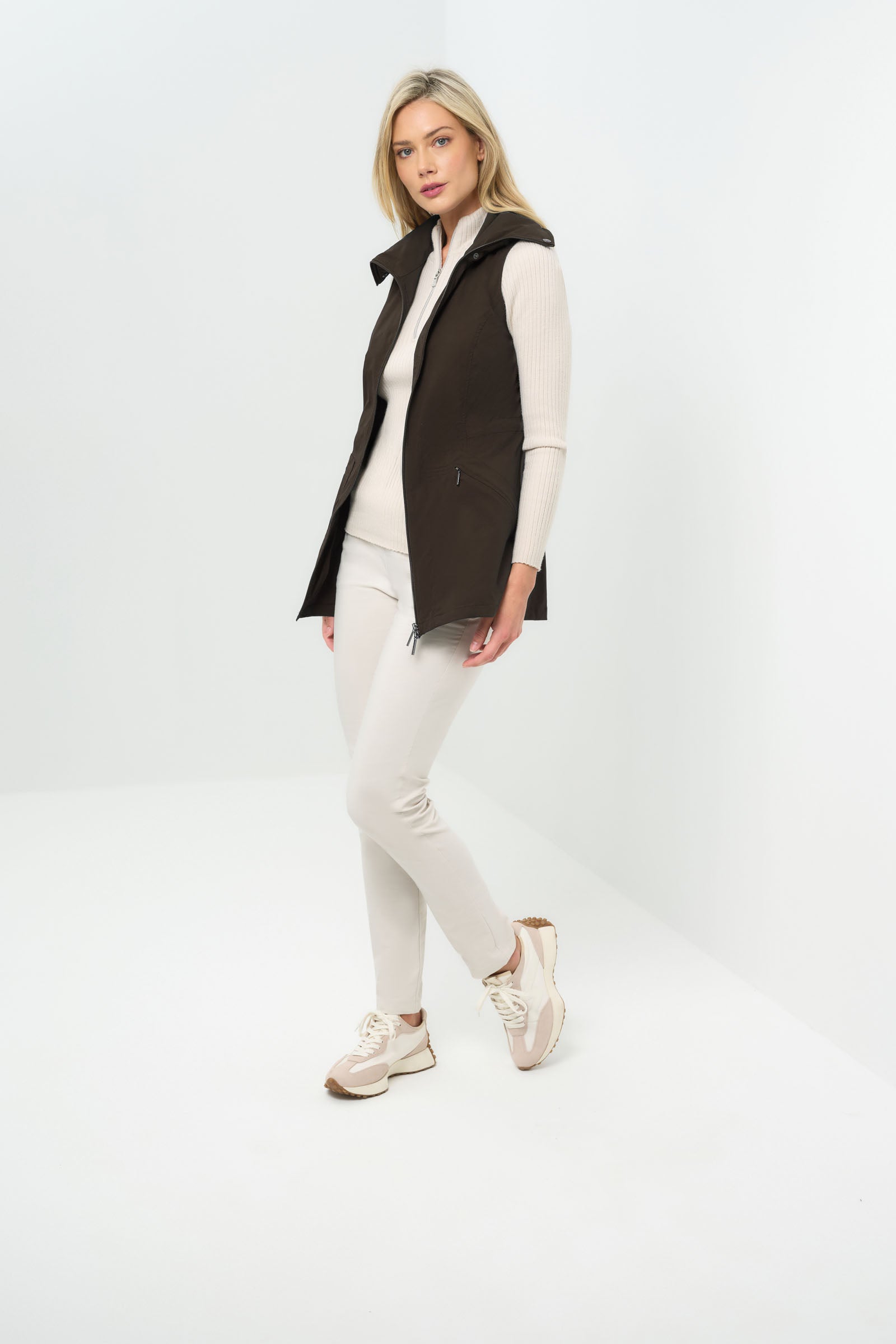 Side view of espresso-colored vested jacket, open at the front with a collar, paired with a white zip-up hoodie and white slim pants.