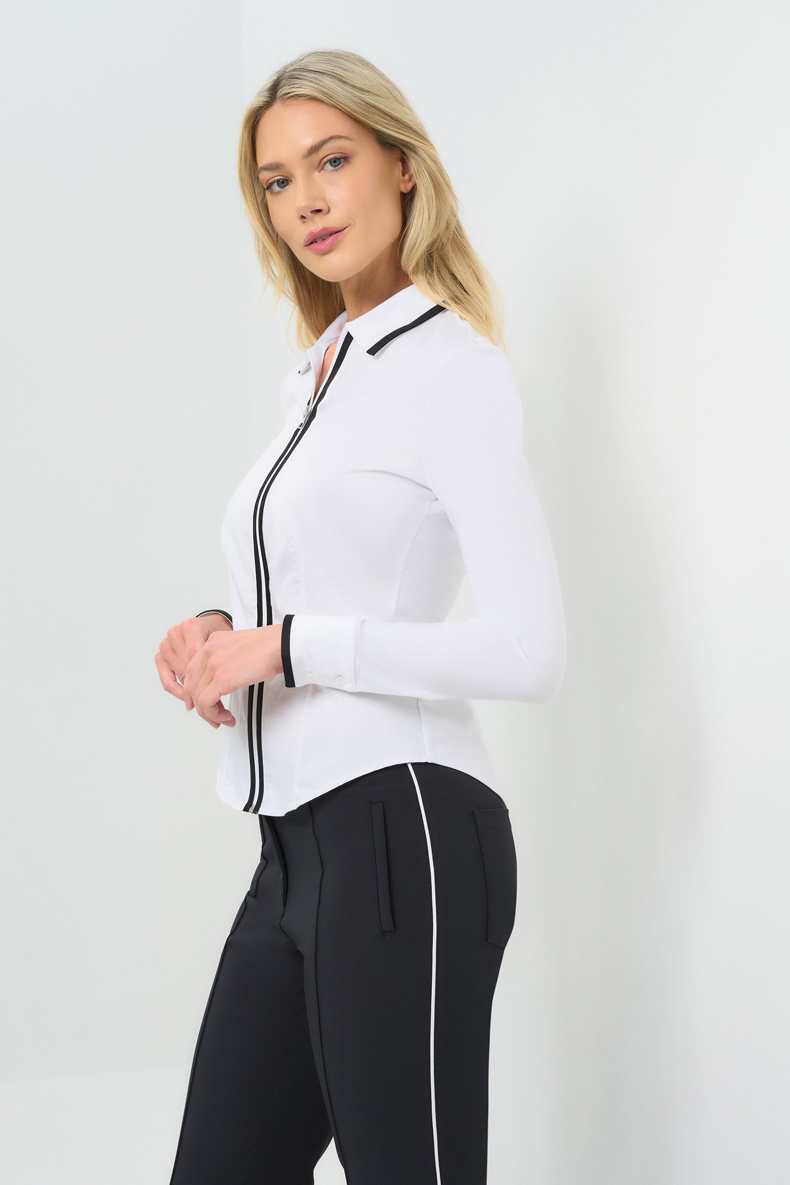 Side view White long-sleeve zip-front blouse featuring a contrasting black trim along the collar, zipper placket, and cuffs.