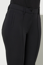 Front view of the Winny Black Pant by Anatomie, showcasing a fitted waistband with a button closure, sleek seam detailing, slim front pockets, and a slightly flared leg. The model pairs the pants with white platform sneakers for a modern, casual look.