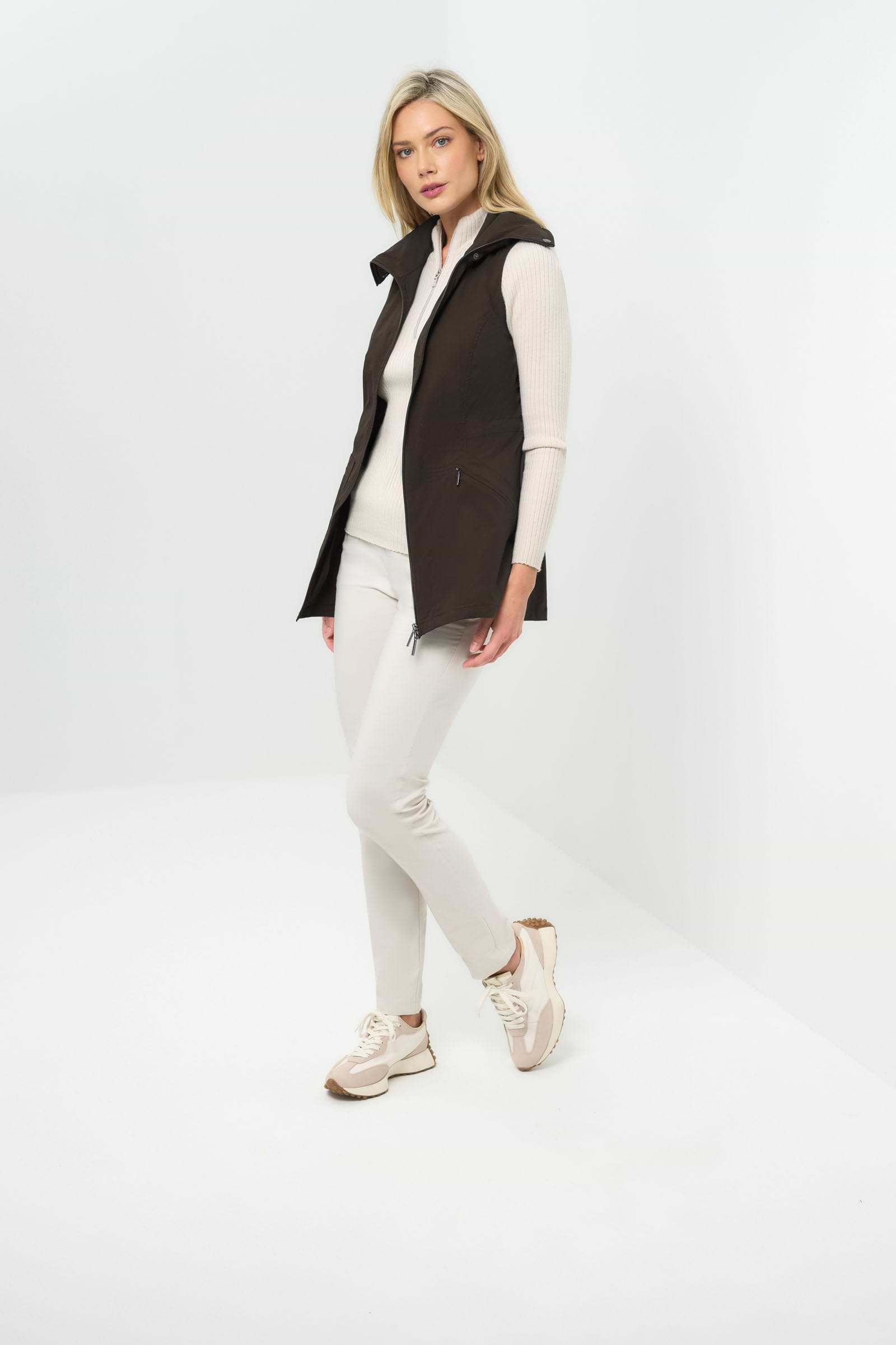 Side view of espresso-colored vested jacket, open at the front with a collar, paired with a white zip-up hoodie and white slim pants.
