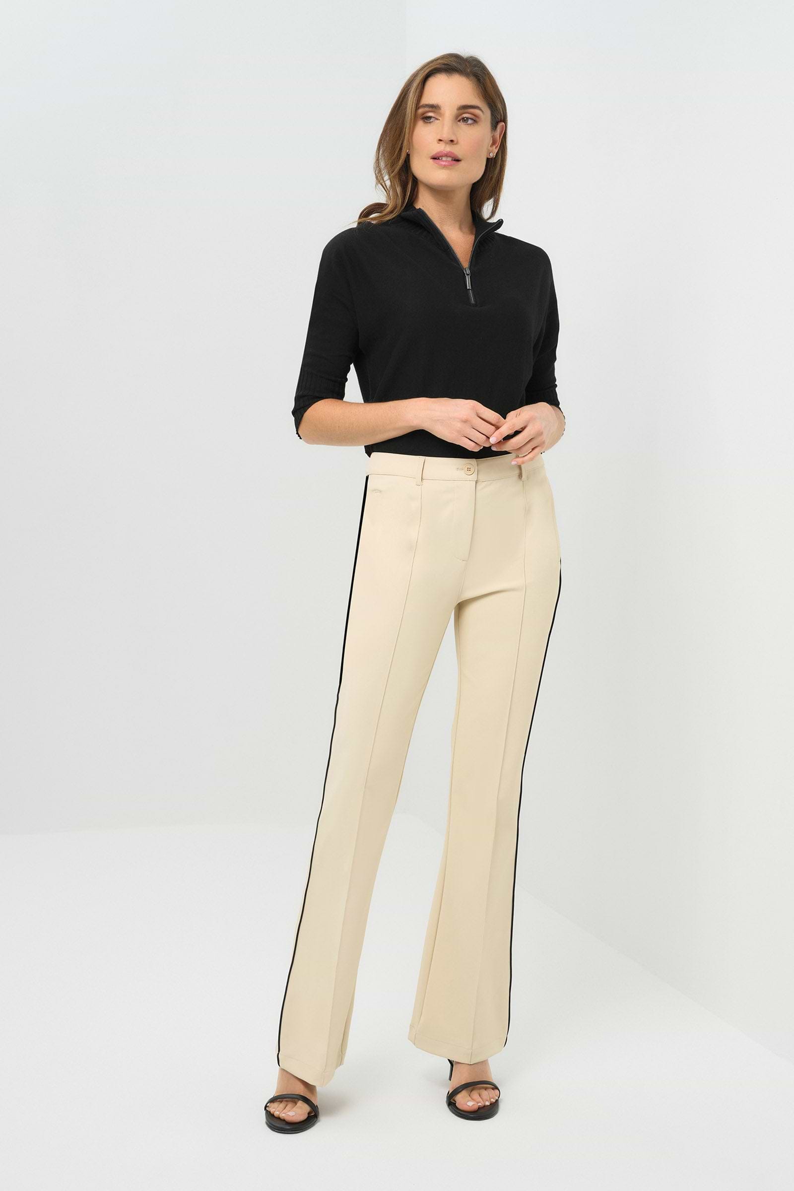 Front view of wheat pants with a black stripe on the side, paired with a black quarter-zip knit top featuring a high collar.