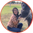 A woman happily playing with a large black dog outdoors.