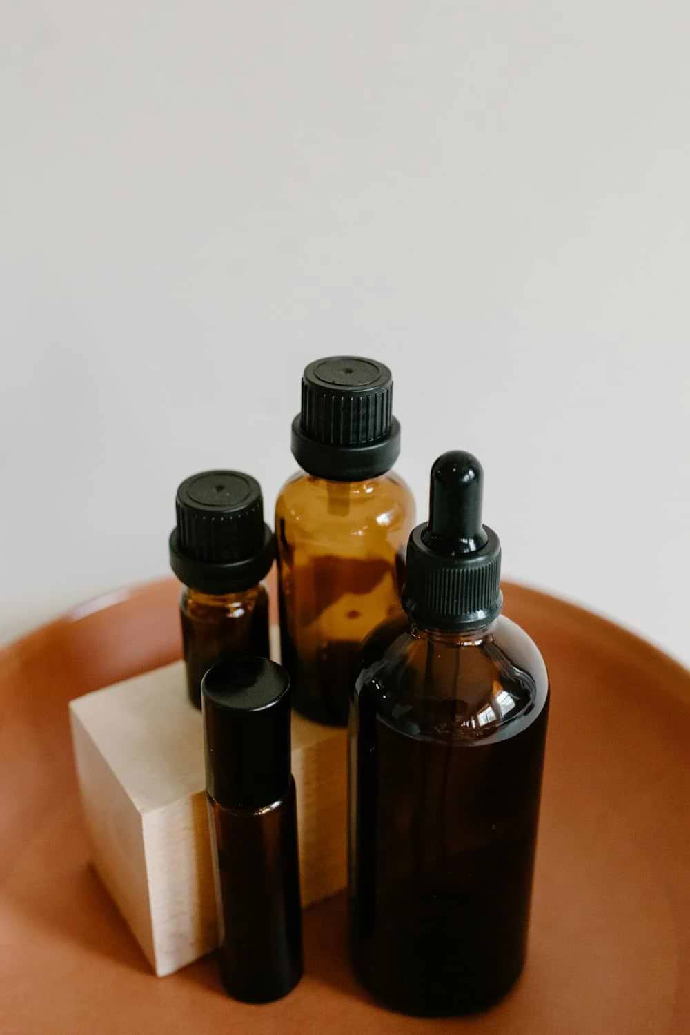 A collection of amber glass bottles, likely for CBD oils, with black caps and droppers, displayed on a wooden block and terracotta surface.