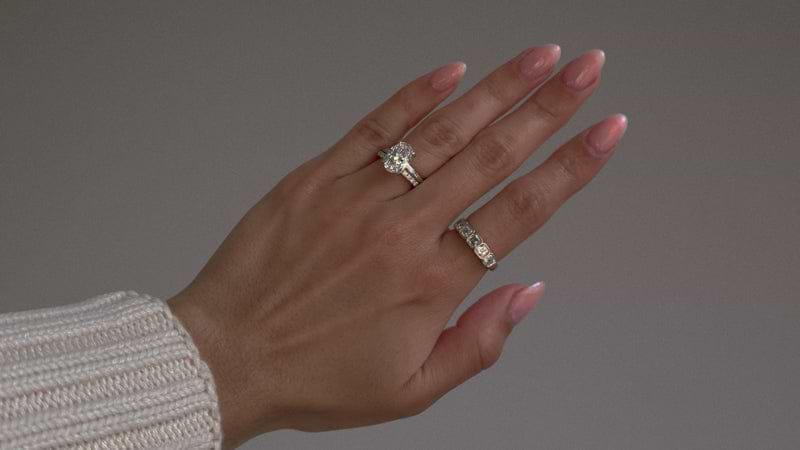 Platinum oval cut engagement ring and diamond pave wedding band on hand.
